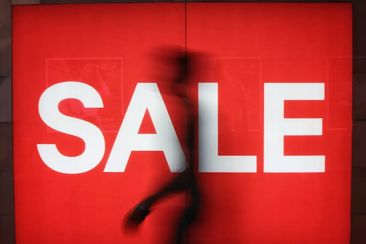 HAULS Journal photo of a blurred shopper walking past a large red SALE sign